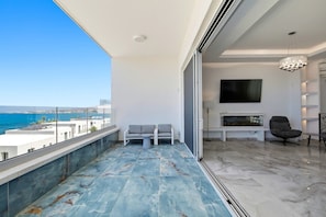 A balcony with a view of the sea, a seating area with a sofa and a table, and a fireplace with a TV mounted on the wall. - Olymp Royal Palace - Ultra Luxury Beachfront House (Paphos)