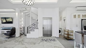 A modern interior with a marble floor, a staircase with decorative railings, a dining area with a glass table, and a kitchen with white cabinets.
