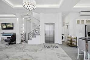 Un interior moderno con piso de mármol, una escalera con barandales decorativos, una zona de comedor con mesa de vidrio y una cocina con gabinetes blancos.
