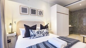 A modern hotel room with a large bed, a bedside table with a lamp, a shower area, and artwork on the wall. - The Paramount | Contemporary Luxury (Johannesburg)