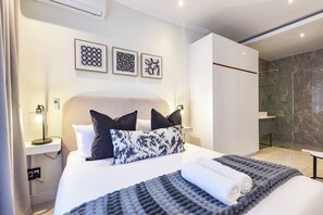 A modern hotel room with a large bed, a bedside table with a lamp, a shower area, and artwork on the wall. - The Paramount | Contemporary Luxury (Johannesburg)