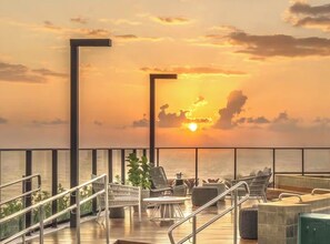 A sunset view from a balcony with outdoor seating and a pool. - Breeze Residence 317 Beachfront Apartment in Bessa (João Pessoa)