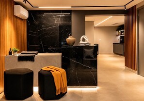 A modern reception area with a marble counter, a sofa, and a small table with a vase and a sculpture. - Breeze Residence 317 Beachfront Apartment in Bessa (João Pessoa)