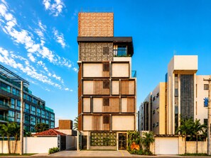 Un edifici modern de diversos pisos amb façanes combinades de vidre i panells de fusta, envoltat de palmeres i altra vegetació.