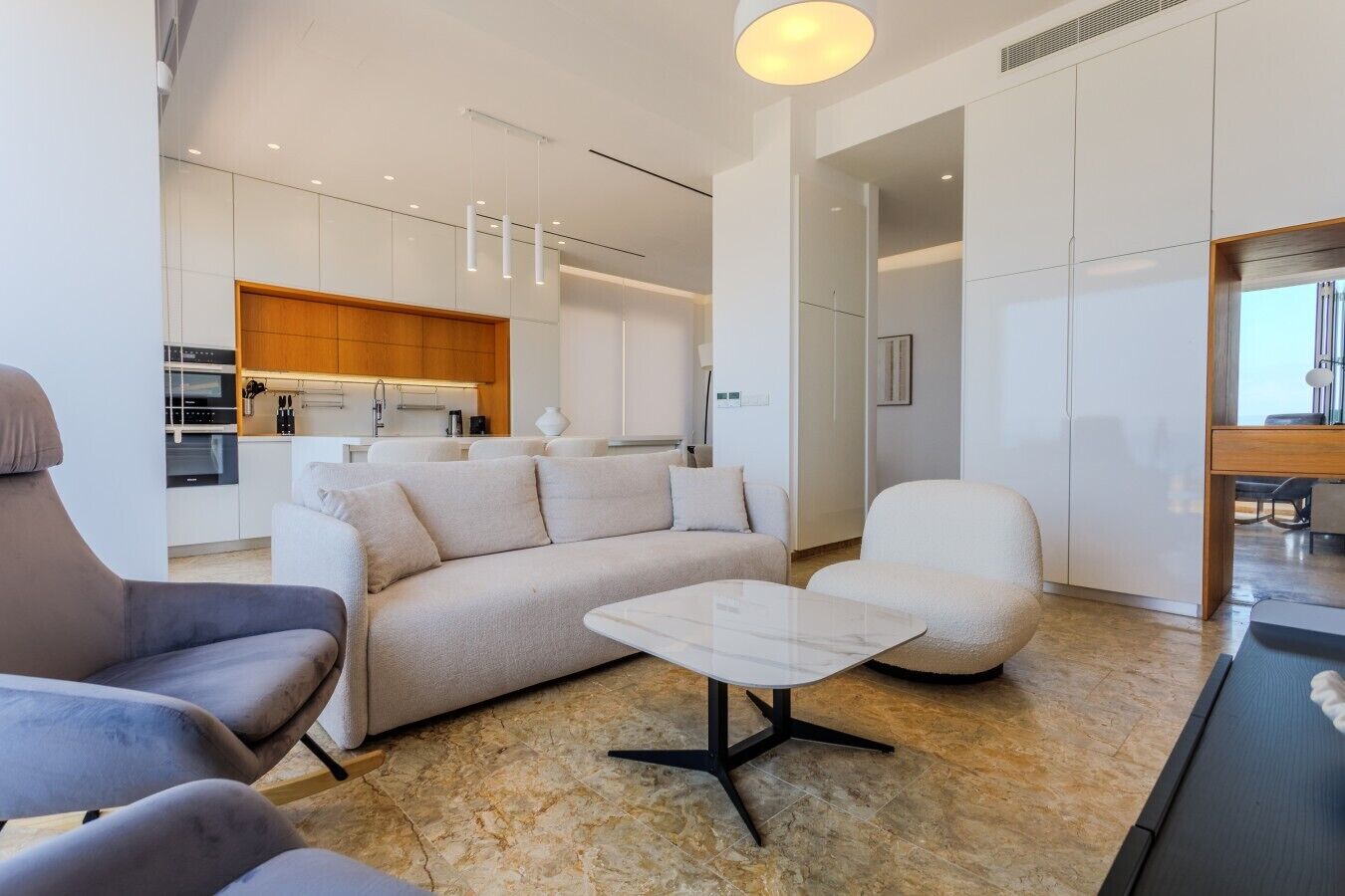 A modern living room with a sofa, armchairs, a coffee table, and a dining area with a table and chairs.