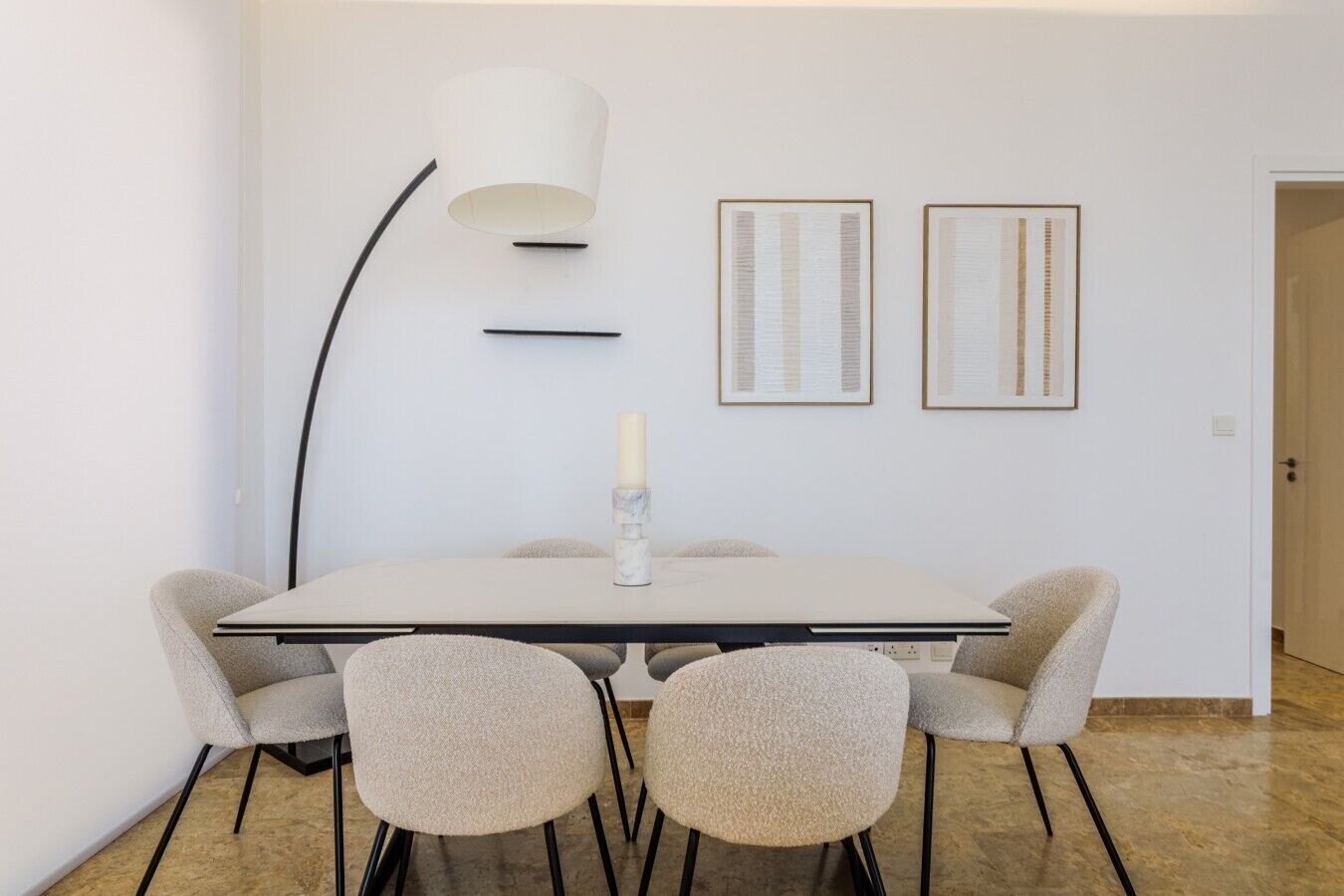 Un espace repas moderne comprenant une table, des chaises, une bougie et des œuvres d’art encadrées accrochées au mur.