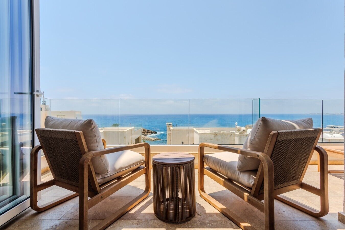 A balcony with two chairs and a small table, overlooking a coastal view.