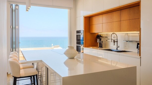Una cocina moderna con una isla grande, armarios de madera y vista al mar.