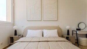 Un dormitorio con una cama, dos mesitas de noche, un tocador, un escritorio con silla, un espejo y arte abstracto en la pared.