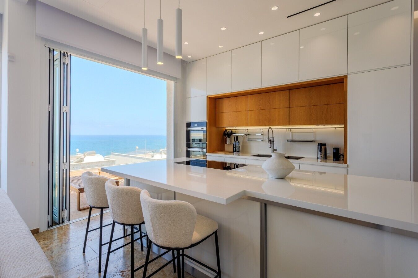 A modern kitchen with a large island, bar stools, and a view of the sea.