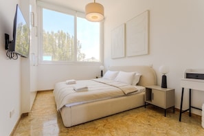 A bedroom with a bed, bedside tables, a TV, and artwork on the wall. - Olymp Luxury Residence - Luxury Beachfront Apartment (Kissonerga)