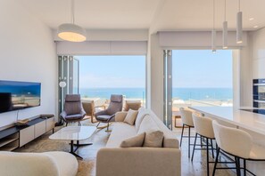 Ein modernes Wohnzimmer mit einem großen Flachbildfernseher, bequemen Sitzgelegenheiten und Meerblick.