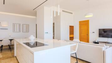 A modern living space with a central island, a sofa, a TV, and a dining area.