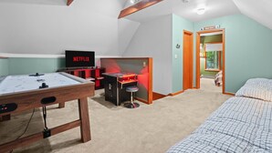 Um quarto acolhedor com uma mesa de futebol de mesa, uma televisão exibindo 'NETFLIX' e uma pequena mesa de jogos com uma luz vermelha.