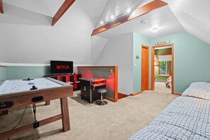 Ein gemütliches Zimmer mit Tischfußball, einem Fernseher, der 'NETFLIX' zeigt, und einem kleinen Spieltisch mit roter Beleuchtung.