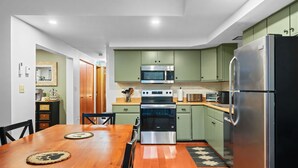Uma cozinha moderna com armários verdes, eletrodomésticos de aço inoxidável e uma mesa de jantar de madeira.