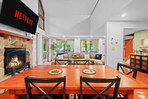 Ein modernes Wohnzimmer mit Kamin, einem an der Wand montierten Fernseher und einem Essbereich mit Holztisch und -stühlen.