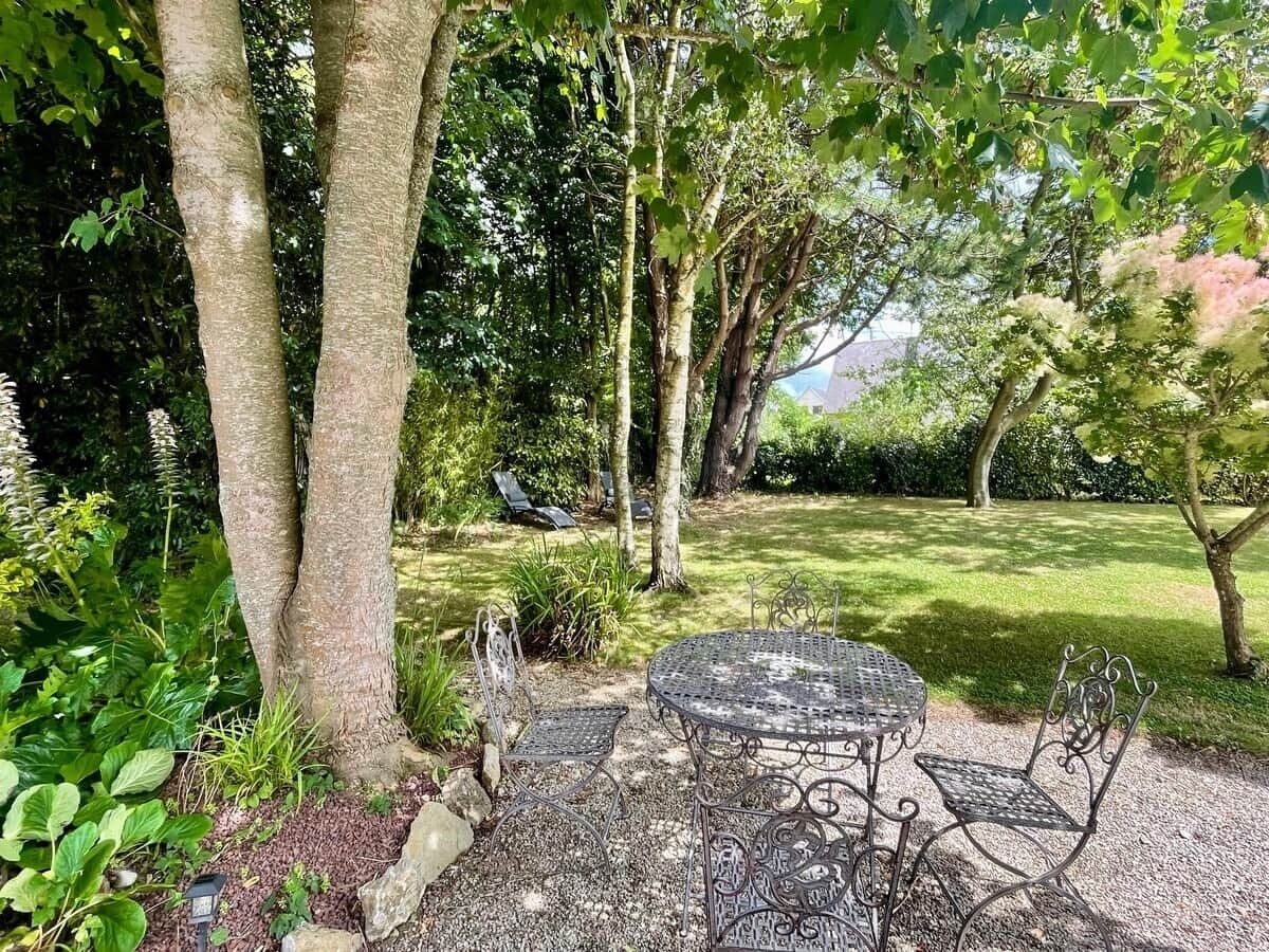 Un jardin avec une table et des chaises en métal, entouré d’arbres et de verdure.