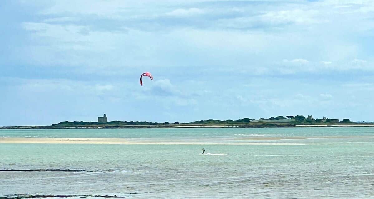 Une plage avec une personne sur une planche de surf et un cerf-volant dans le ciel.