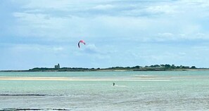 A beach with a person on a surfboard and a kite in the sky.