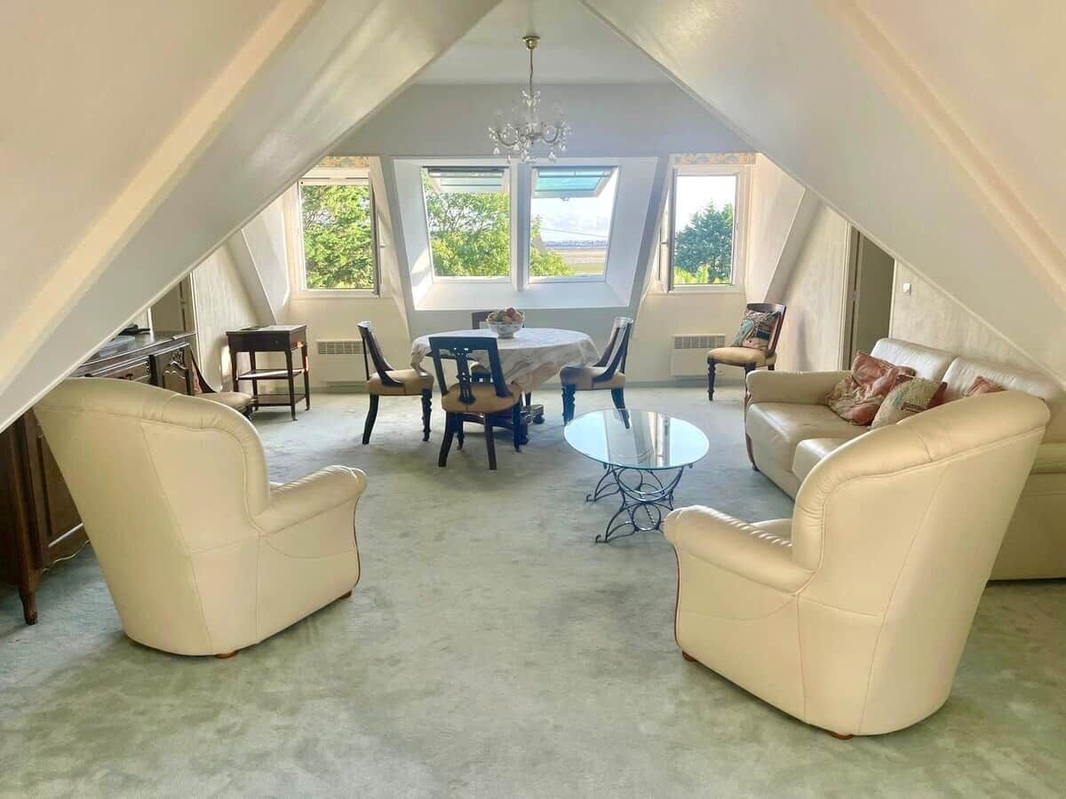 Een zolderkamer met hoge plafonds, een eettafel met stoelen, twee banken en een kroonluchter.
