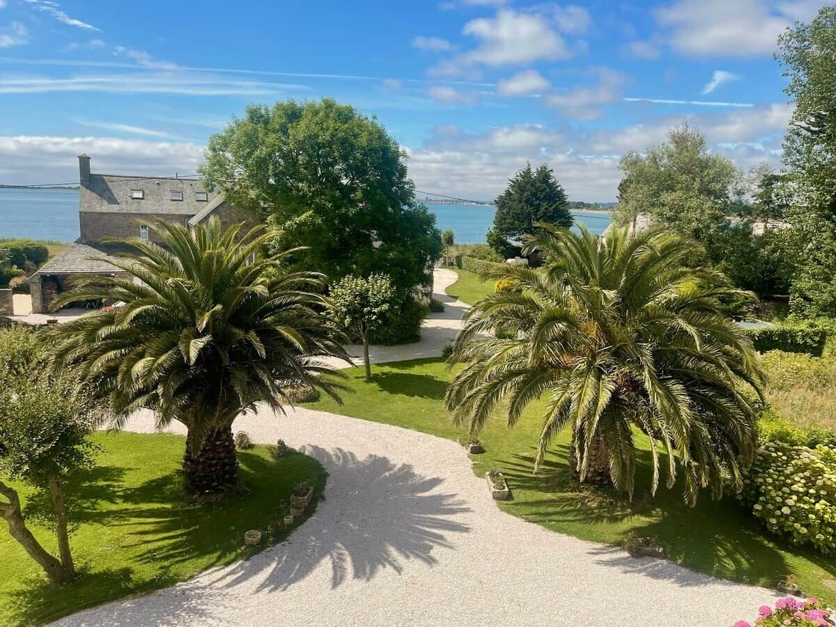 Un sentier menant à une maison d’où l’on a vue sur la mer, et où l’on aperçoit un pont au loin.