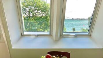 Een kamer met een ontbijttafel, een schaal fruit en uitzicht op een wateroppervlak door twee ramen.