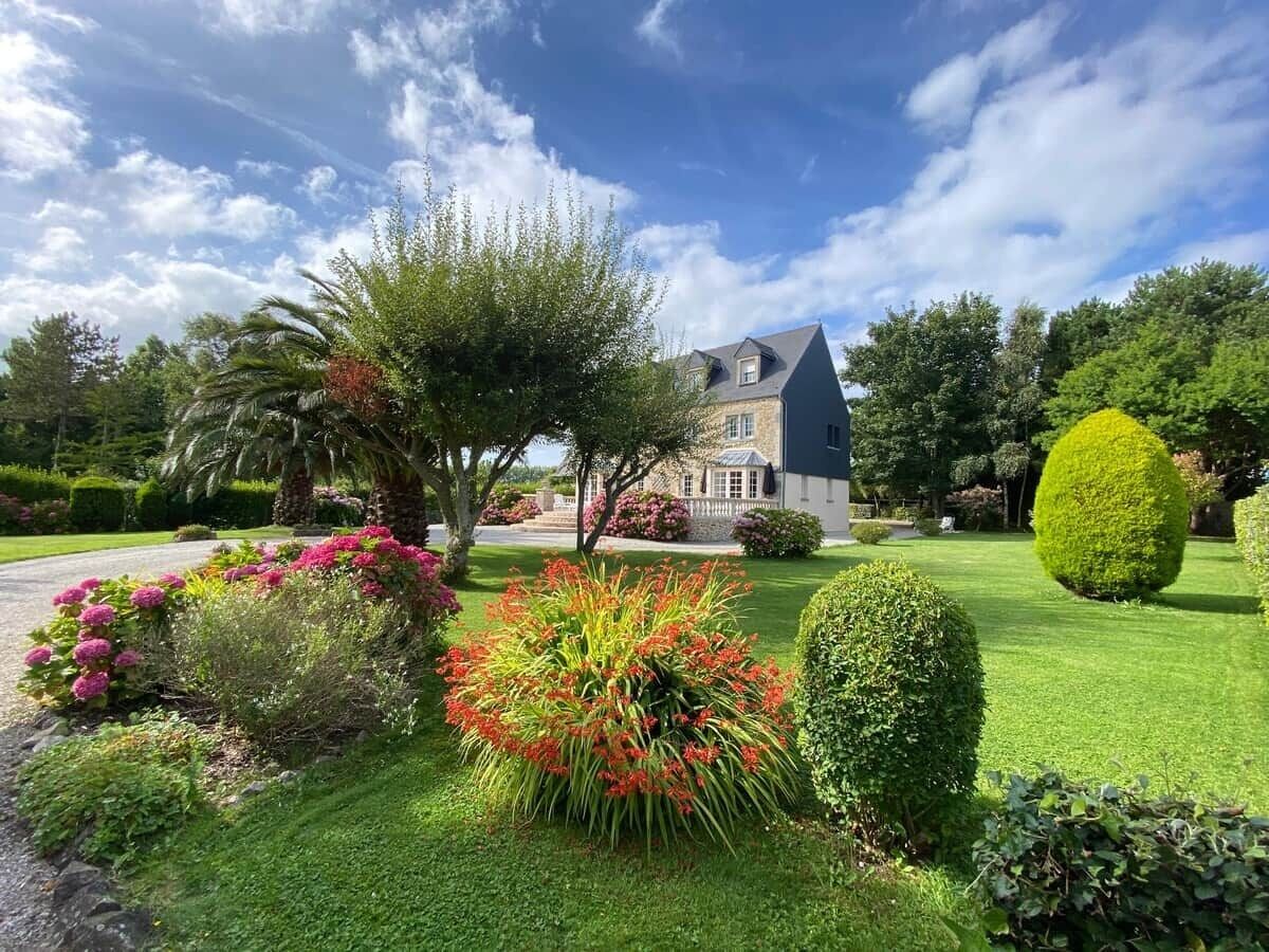 Un jardin bien entretenu, avec différentes espèces de plantes, et une maison en arrière-plan.