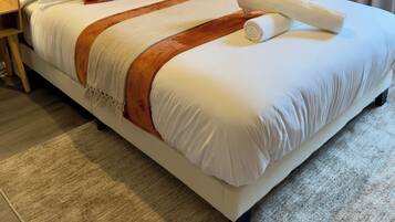 A neatly made bed with white linens, a brown throw blanket, and a rolled towel. There are two nightstands with lamps, and the room has a neutral color scheme.