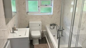Un baño con inodoro, bañera, ducha y una ventana sobre el inodoro.