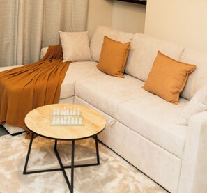 A modern living room with a white sofa, two brown cushions, a wooden coffee table with chess pieces, and a beige rug. - St Julian House- Town Centre- Castle Park- Hot Tub (Colchester)