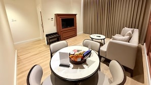 Una sala de estar moderna con una mesa redonda, dos sofás, una televisión y un amplio ventanal con cortinas.