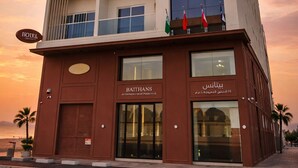 Un hotel de varios pisos con balcones, un restaurante en la planta baja y banderas en el techo.