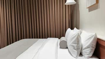 A hotel room with a bed, curtains, a wall-mounted light, and a framed picture.