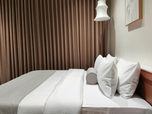 A hotel room with a bed, curtains, a wall-mounted light, and a framed picture.