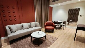 Una sala de estar moderna con un sofá, una silla roja, una mesa de centro redonda y un comedor con mesa y sillas.