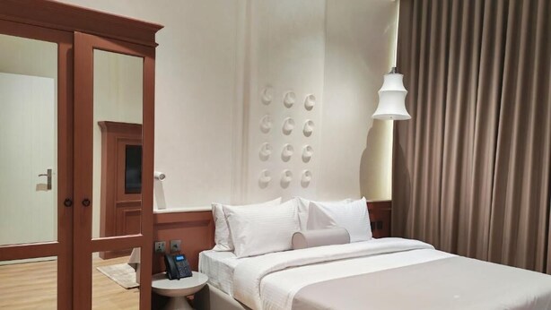 Una habitación de hotel con cama, mesita de noche y armario con espejo.