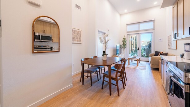 A modern kitchen with built-in appliances, a dining area with a wooden table and chairs, and a view through large windows. - Vibrant King 1B1B｜Pool & Spa｜Smart 4K TVs (Montclair)
