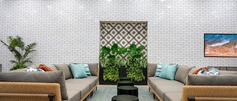 A modern lounge area with two sofas, a central plant, and a patterned wall.