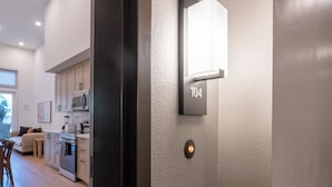 A modern kitchen with built-in appliances, a dining area with a sofa and chairs, and a wall-mounted light fixture with the number 104. - Vibrant King 1B1B｜Pool & Spa｜Smart 4K TVs (Montclair)