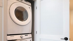 A laundry room with two Samsung washing machines and a white door with a vent. - Vibrant King 1B1B｜Pool & Spa｜Smart 4K TVs (Montclair)