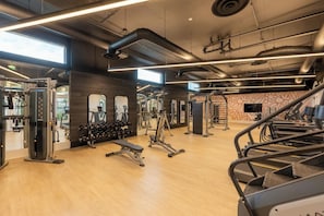Ein Fitnessraum mit unterschiedlichen Trainingsgeräten, Holzböden und großen Fenstern für natürliches Licht.