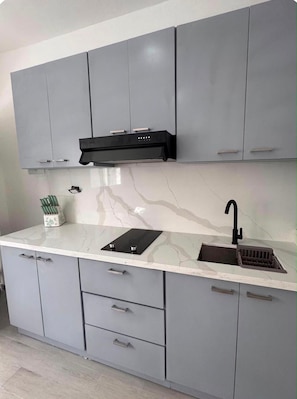 A modern kitchen with grey cabinets, a black range hood, a sink with a black faucet, and a marble countertop. - Bayahibe Stay (Bayahíbe)