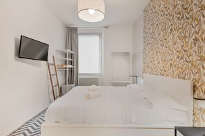 Une chambre d’hôtel moderne dotée d’un grand lit, d’un téléviseur fixé au mur, d’une armoire et d’une fenêtre avec des rideaux.