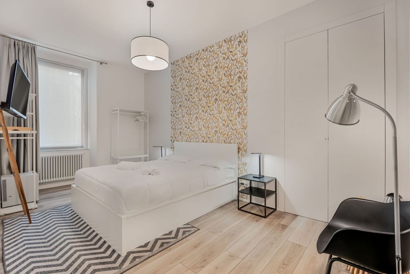 Une chambre à coucher moderne, avec un lit, des tables de chevet, un bureau, une chaise, un radiateur et une fenêtre avec des rideaux.