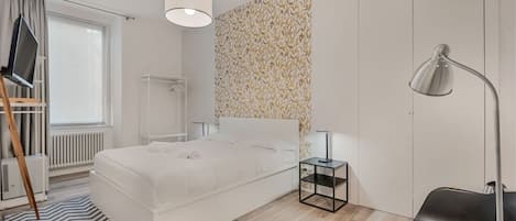 Un dormitorio moderno con cama, mesitas de noche, un escritorio, una silla, un radiador y una ventana con cortinas.