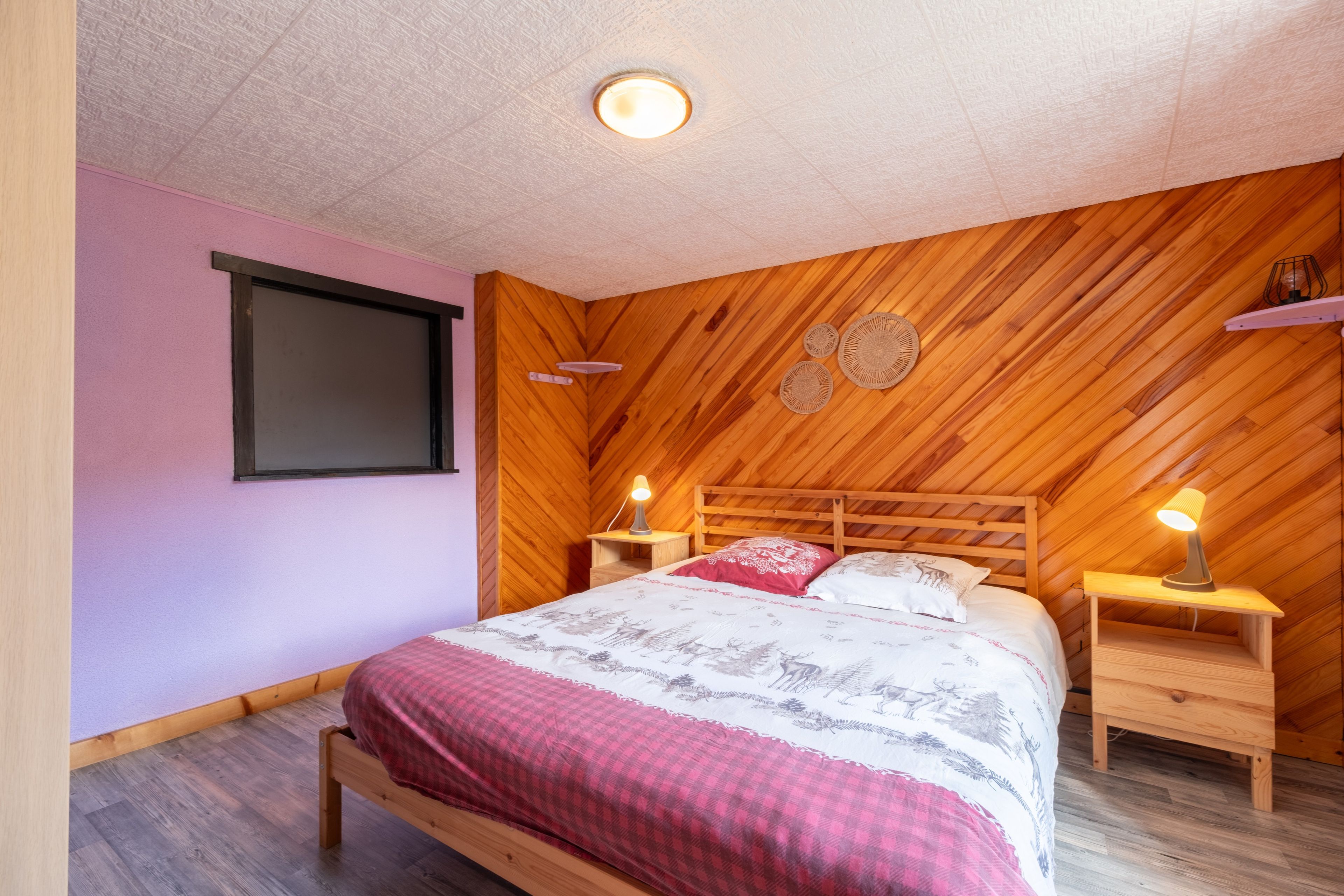 A bedroom with a wooden headboard, a bed with patterned bedding, bedside lamps, and a wall-mounted shelf.