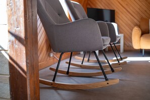 A set of three rocking chairs with black legs and grey fabric, positioned in a room with wooden walls and a television in the background.