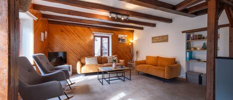 A cozy living room with wooden beams, a television, two sofas, and a bookshelf.