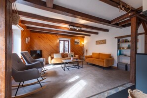A cozy living room with wooden beams, a television, two sofas, and a bookshelf.
